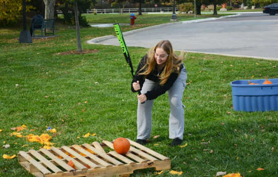 Action shot of a student preparing to smash a pumpkin with a baseball bat outside on the grass