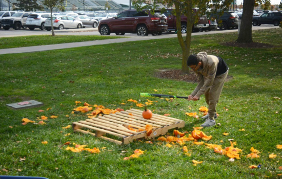 Action shot of a student preparing to smash a pumpkin with a baseball bat outside on the grass